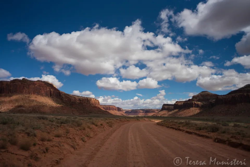 Cumulus clouds over a red dirt road running into Moab canyon country
